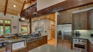 A spacious kitchen with wooden cabinets, a stainless steel refrigerator, and a large island with a built-in oven. - Holly Hideaway - TLUXP (Tahoe City)