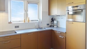 A compact kitchen with a window, stainless steel appliances, and wooden cabinets. - Oesterbaai - 8 personen (Wemeldinge)