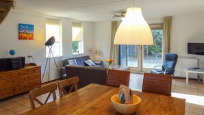 A modern living room with a wooden dining table, a sofa, and a TV. - Oesterbaai - 8 personen (Wemeldinge)