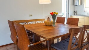 A wooden dining table with a bowl and vase of flowers, surrounded by chairs with cushioned seats. - Oesterbaai - 8 personen (Wemeldinge)