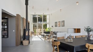 Ett modernt vardagsrum med en centralt placerad öppen spis, en matplats med ett svart bord och stolar samt en mysig sittgrupp med en soffa och fåtöljer.