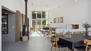 A modern living space with a central fireplace, a dining area with a black table and chairs, and a cozy seating area with a sofa and chairs.