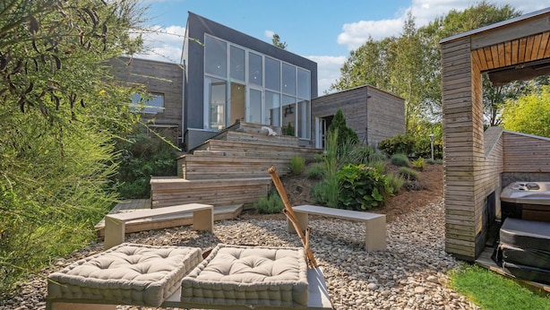 Ett modernt hus med ett stort glasfönster, en träaltan och utemöbler.