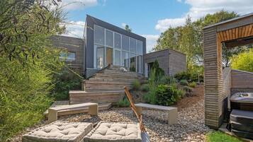 A modern house with a large glass window, wooden deck, and outdoor seating.