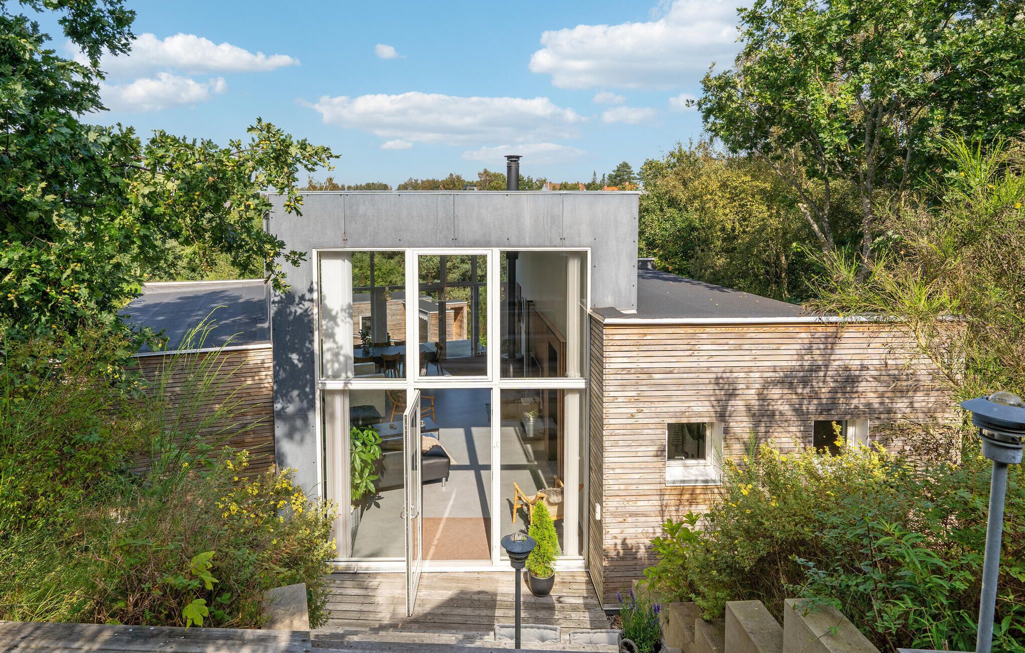 A modern house with a large glass front, a wooden deck, and a chimney.