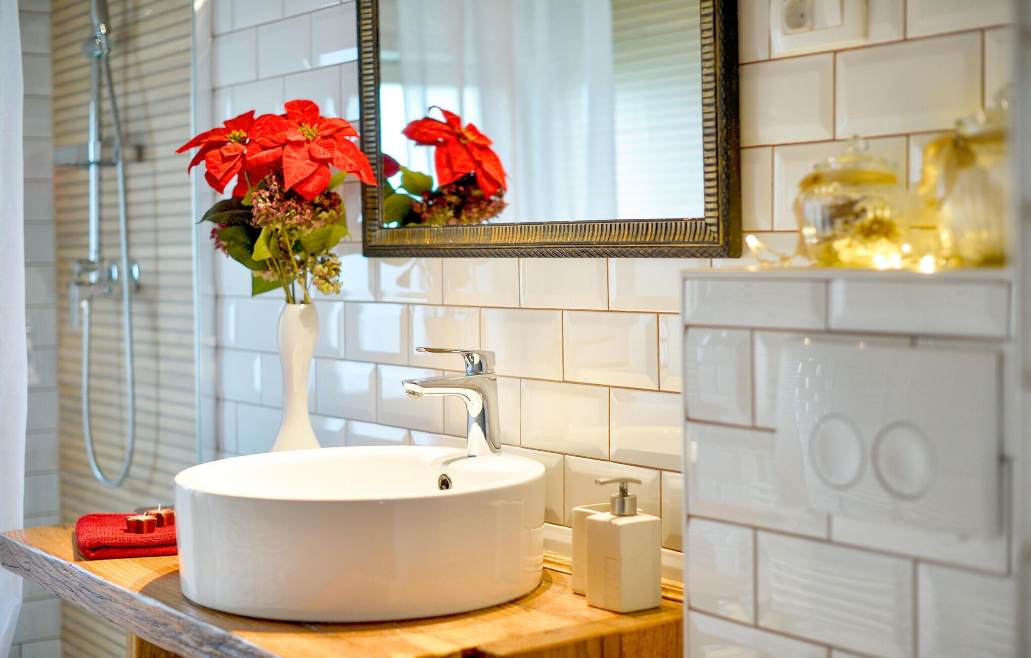 Un baño con un lavamanos blanco, un espejo y un florero con flores rojas.