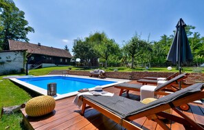 Een achtertuin met een zwembad, lounge stoelen en een houten terras.