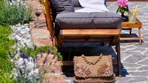 A wooden lounge chair with a cushion, a woven bag, and a small table with a drink and flowers. - Gorgeous home in Kupljenovo (Kupljenovo)