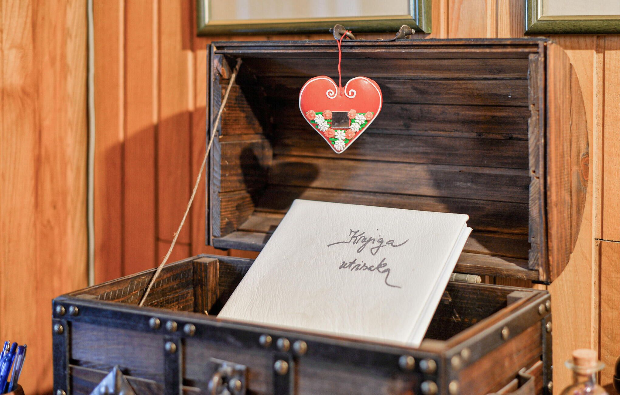 A wooden chest with a heart-shaped ornament hanging above it. Inside the chest, there is a white envelope with handwritten text.
