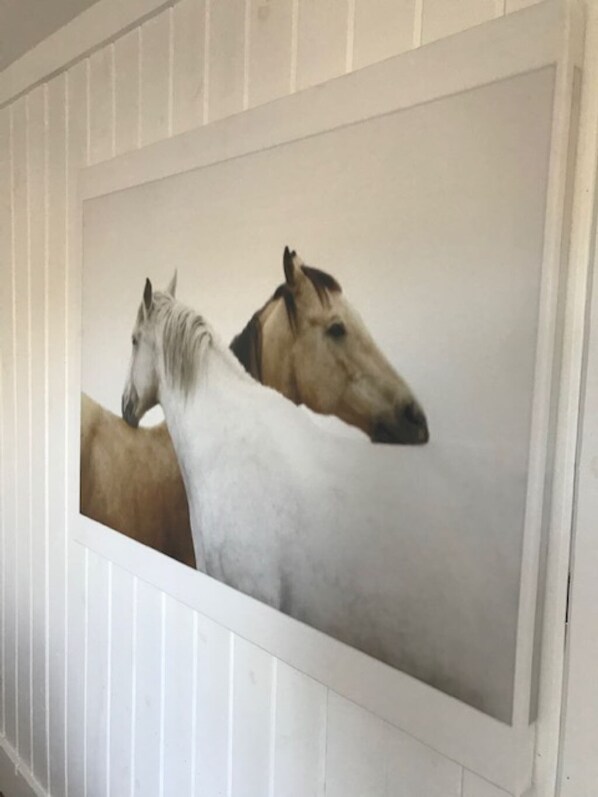 Un cuadro con dos caballos sobre un muro blanco.