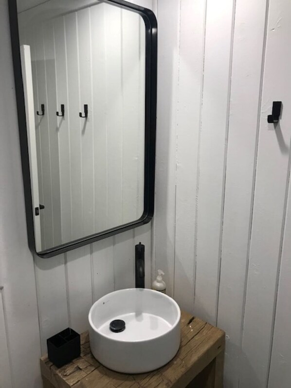 Un baño con un lavamanos blanco, un espejo con marco negro y paneles de madera en las paredes.