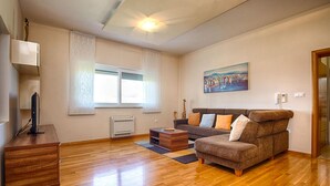 A living room with a brown sofa, a wooden coffee table, a TV on a stand, a painting on the wall, and a window with sheer curtains. - Amazing home in Kozino (Kozino)
