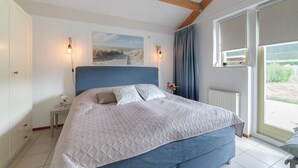 A bedroom with a large bed, a painting, two wall-mounted lights, a window with curtains, and a view of greenery outside. - Awesome home in Wemeldinge with sauna (Wemeldinge)