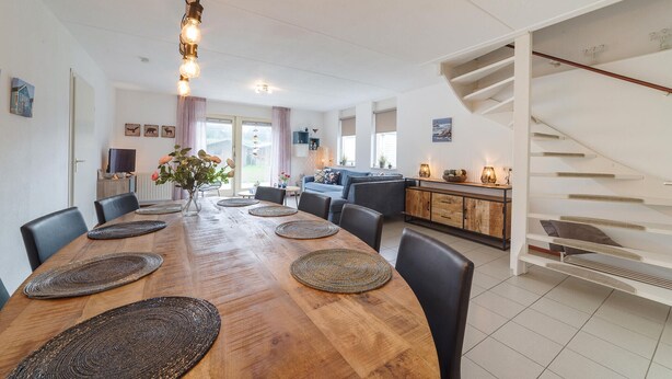 A modern dining area with a wooden table, black chairs, and woven placemats. There is a staircase to the right and a view of the outdoors through the windows. - Awesome home in Wemeldinge with sauna (Wemeldinge)