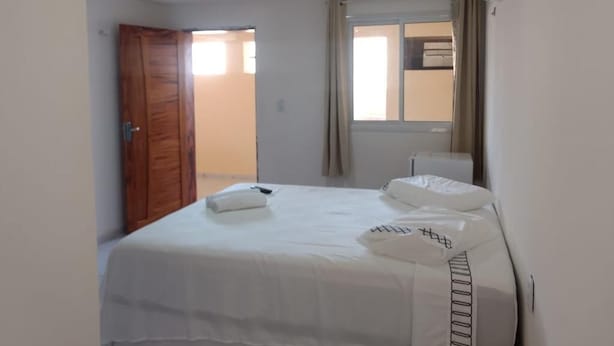 A bedroom with a bed, a window with curtains, a door, and a wall-mounted air conditioning unit. - Barcelona Beach Residence (Aracati)