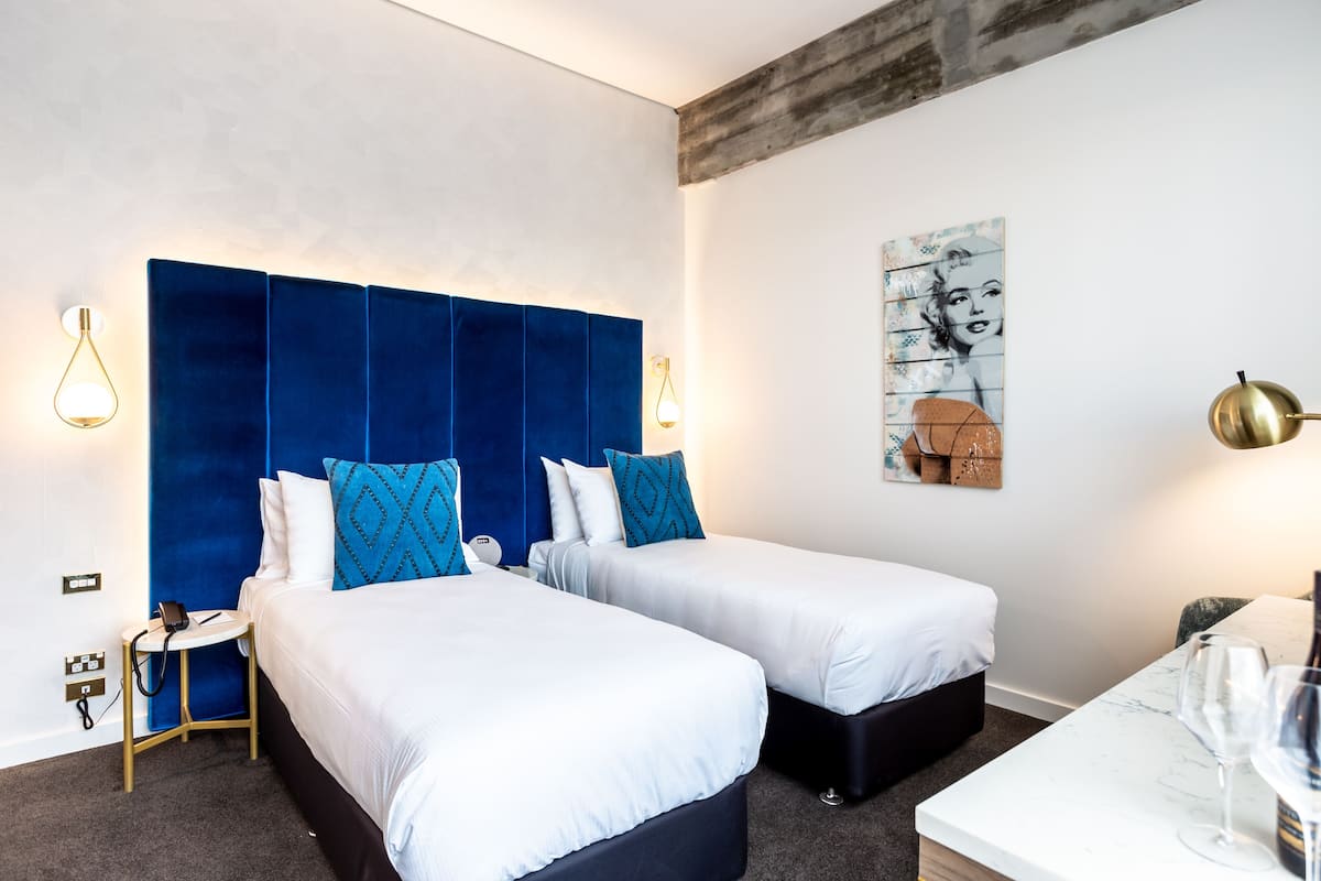 Habitación de hotel con dos camas, una mesita de mármol y un cuadro en la pared.