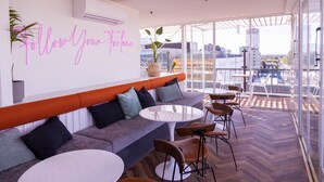 A modern lounge area with a sofa, round tables, and a neon sign. - The Muse Christchurch, Art Hotel (Christchurch)