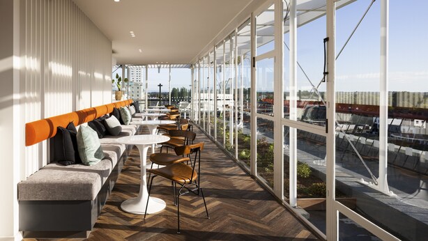 A modern interior with a long bench, tables, and chairs, large windows offering a view of the city. - The Muse Christchurch, Art Hotel (Christchurch)
