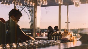 A bar area with hanging light fixtures, a counter with glasses, and a view of the outside. - The Muse Christchurch, Art Hotel (Christchurch)