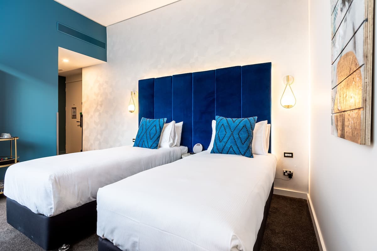 Habitación de hotel con dos camas, una pared azul de acento y una lámpara moderna.