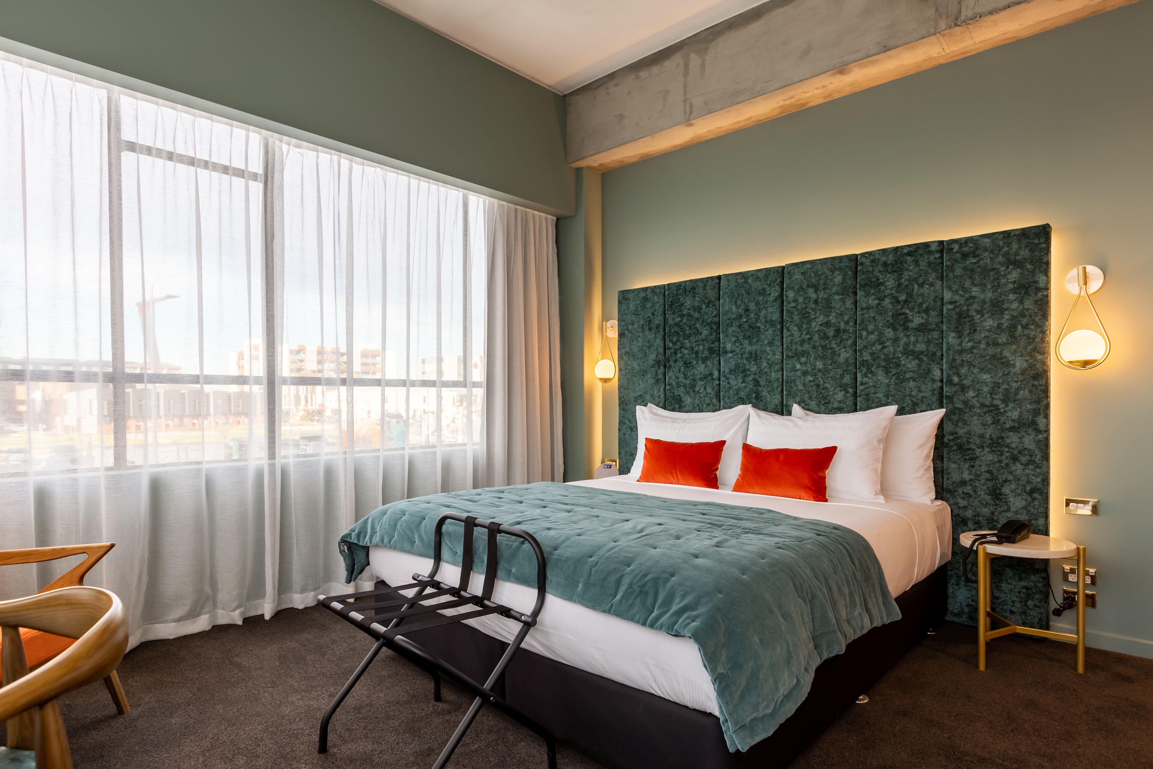 Una habitación de hotel con una cama, una silla, una mesita de noche y una ventana con cortinas.