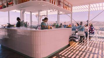 A bar area with a high counter, bottles, and glasses. There are people seated and standing around.