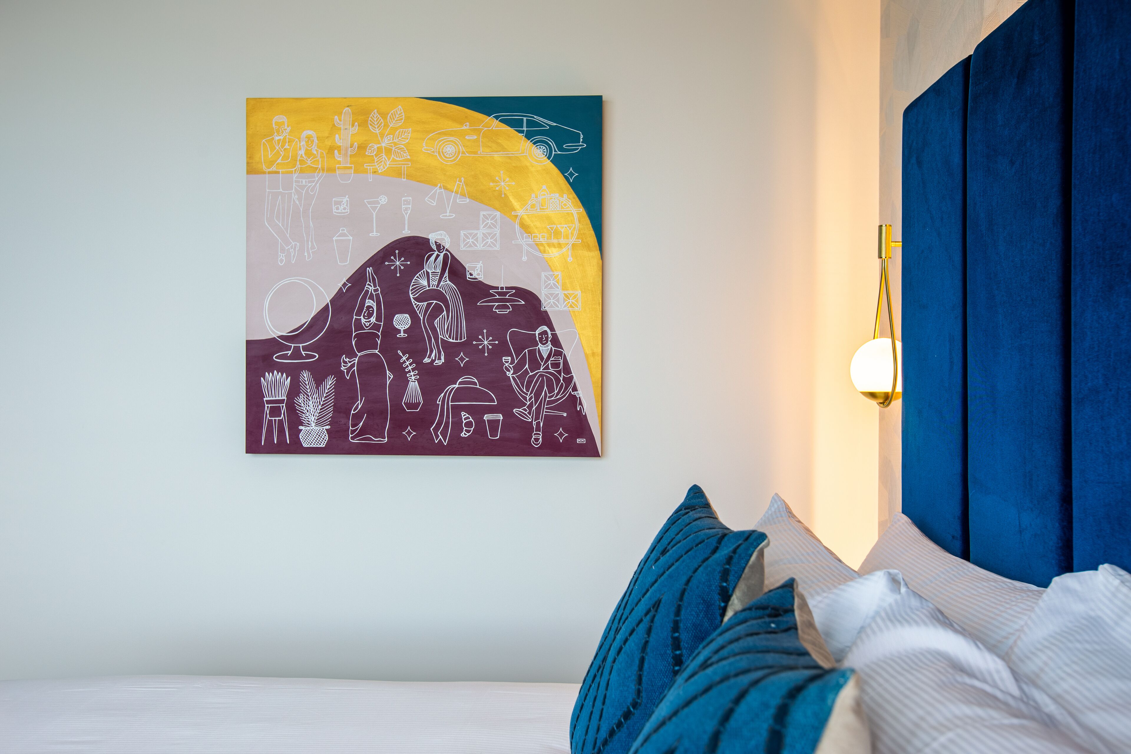A bedroom with a bed, a blue headboard, a wall-mounted artwork, and a wall-mounted light fixture.