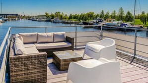 A marina with boats docked, a lounge area with wicker furniture and a glass-top table, and a clear view of the water. - Amazing ship in Aalsmeer with harbor view (Aalsmeer)