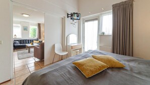 Une chambre à coucher avec un lit, deux oreillers, un bureau avec une chaise, un miroir et un téléviseur fixé au mur.