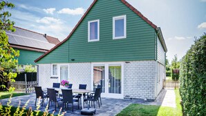 Une maison à deux étages, dotée d’un toit végétalisé, d’une façade en briques blanches et d’une terrasse avec une table et des chaises.