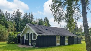 A small, dark-colored building with a sloped roof, surrounded by a grassy area and trees.