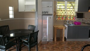 Una cuina compacta amb nevera, una taula de dinar amb caires i una finestra amb cortina.