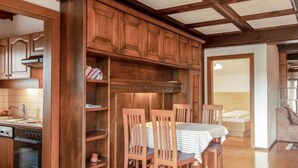 Una cocina de madera con alacenas integradas, una mesa de comedor con sillas y vistas al dormitorio contiguo.