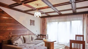 Una sala de estar con un sofá seccional, una mesa de centro de madera y una silla de madera. Se ve una escalera con barandas de madera a la izquierda.