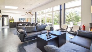 Un salon moderne avec un canapé d’angle, une table basse et une cheminée. De grandes fenêtres laissent entrer la lumière naturelle et offrent une vue sur l’extérieur.
