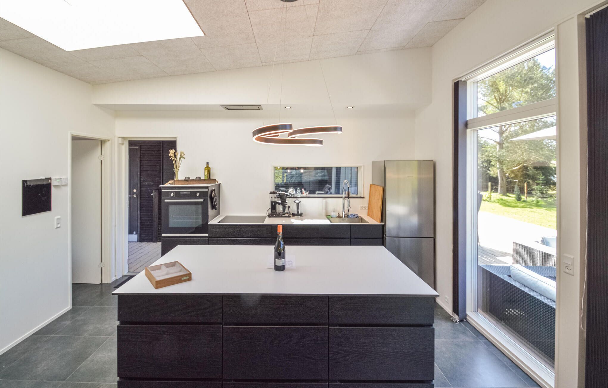 A modern kitchen with a central island, a built-in oven, and a large window providing a view of the outdoors.