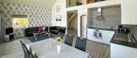Een modern appartement met een eethoek, keuken, woonkamer en een trap naar een entresol.