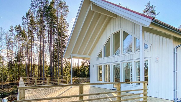 Una baita moderna con veranda in legno, ampie finestre e facciata bianca.