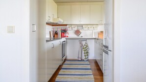 A narrow kitchen with white cabinets, a striped rug, and a hanging kitchen towel.