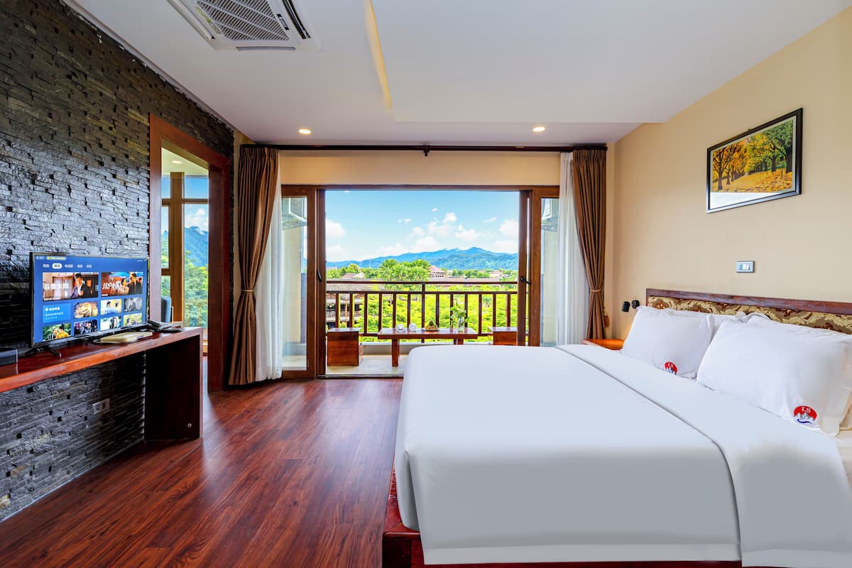 Ein Hotelzimmer mit einem großen Bett, einem Fernseher auf einer Holzkonsole und einem Balkon mit Bergblick.