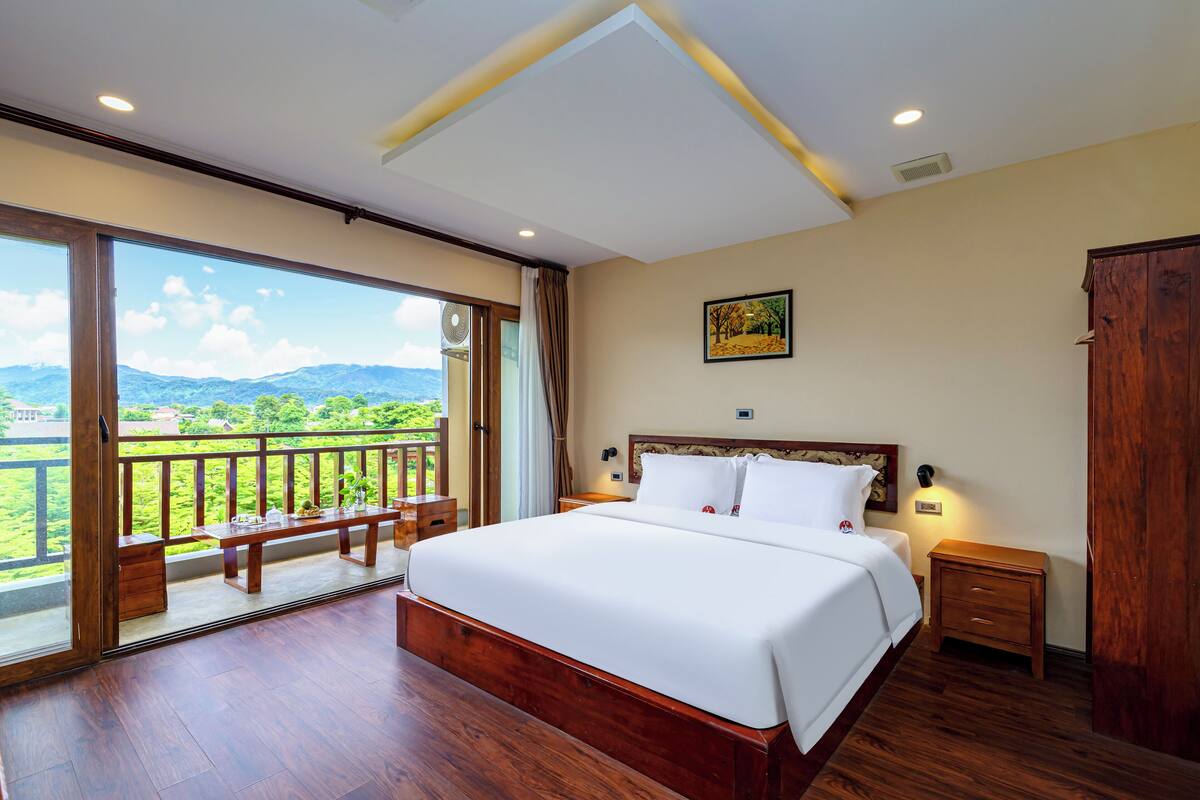 Ein Schlafzimmer mit einem großen Bett, Holzboden, einem Balkon mit Bergblick und einem Holzschrank.