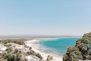 A coastal landscape with a beach, clear sky, and distant mountains. - Mavis - Little Cove (Noosa Heads)