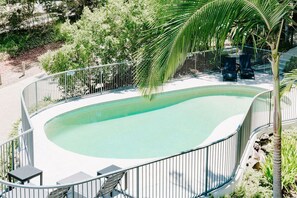 A swimming pool with a curved edge, surrounded by a metal fence, and two lounge chairs.