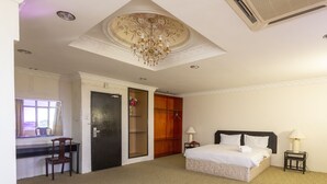 Een hotelkamer met een bed, nachtkastjes, een bureau, een stoel, een kledingkast en een plafond met een kroonluchter.