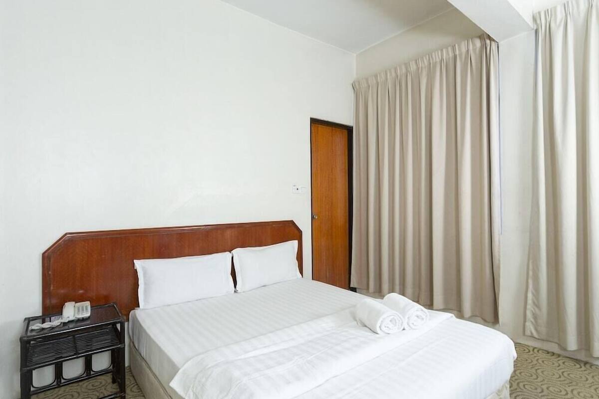 A hotel room with a wooden headboard bed, white linens, a bedside table with a phone, and a window with curtains.