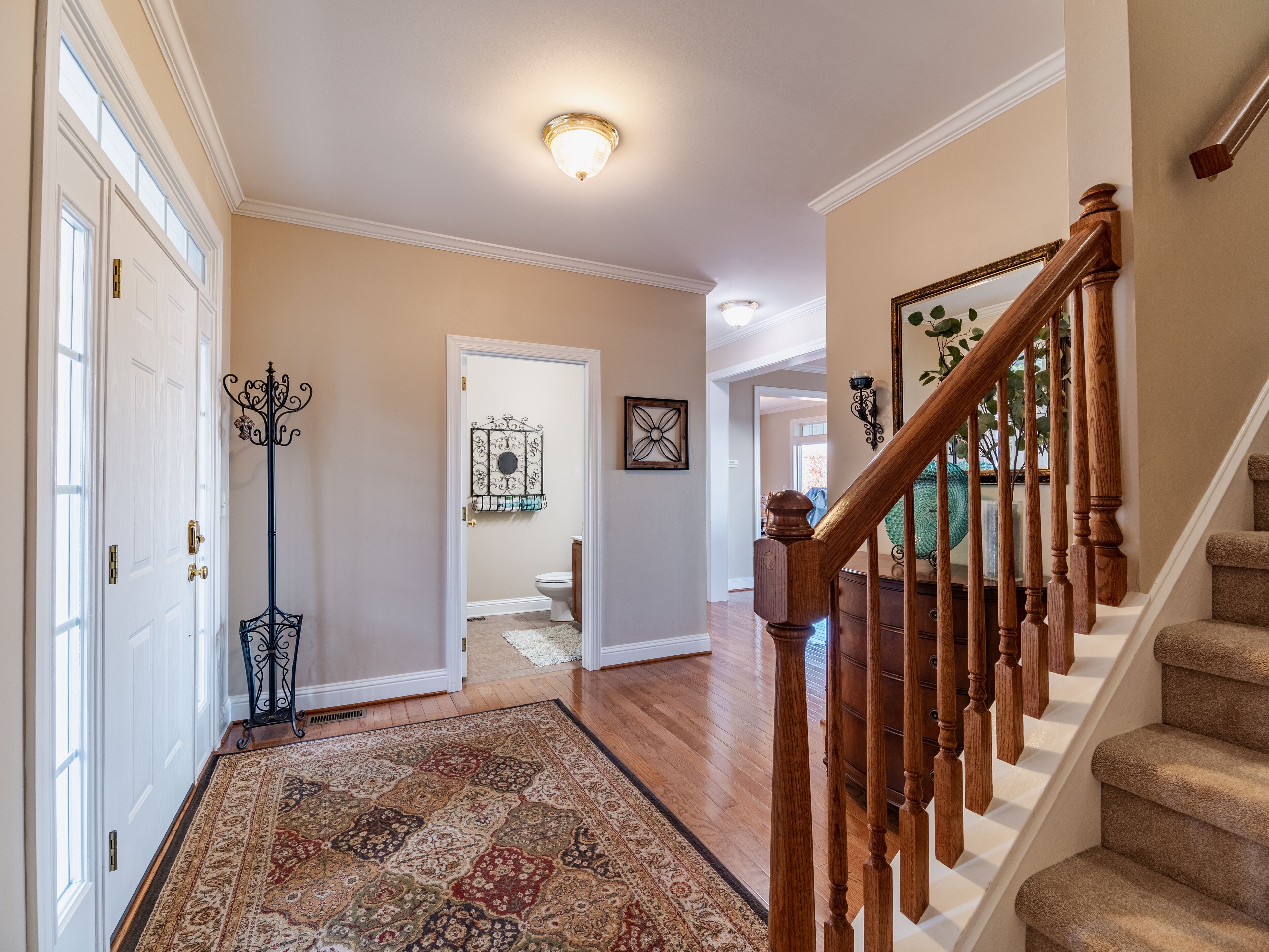 Un couloir avec un tapis à motifs, un escalier en bois et une porte donnant accès à une salle de bain.
