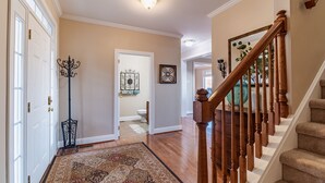 A hallway with a patterned rug, a wooden staircase, and a door leading to a bathroom.