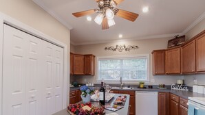 A kitchen with wooden cabinets, a central island with a fruit platter, a ceiling fan, and a window with blinds.