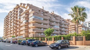 Un edificio residencial de varios pisos con balcones, estacionamiento y una palmera.