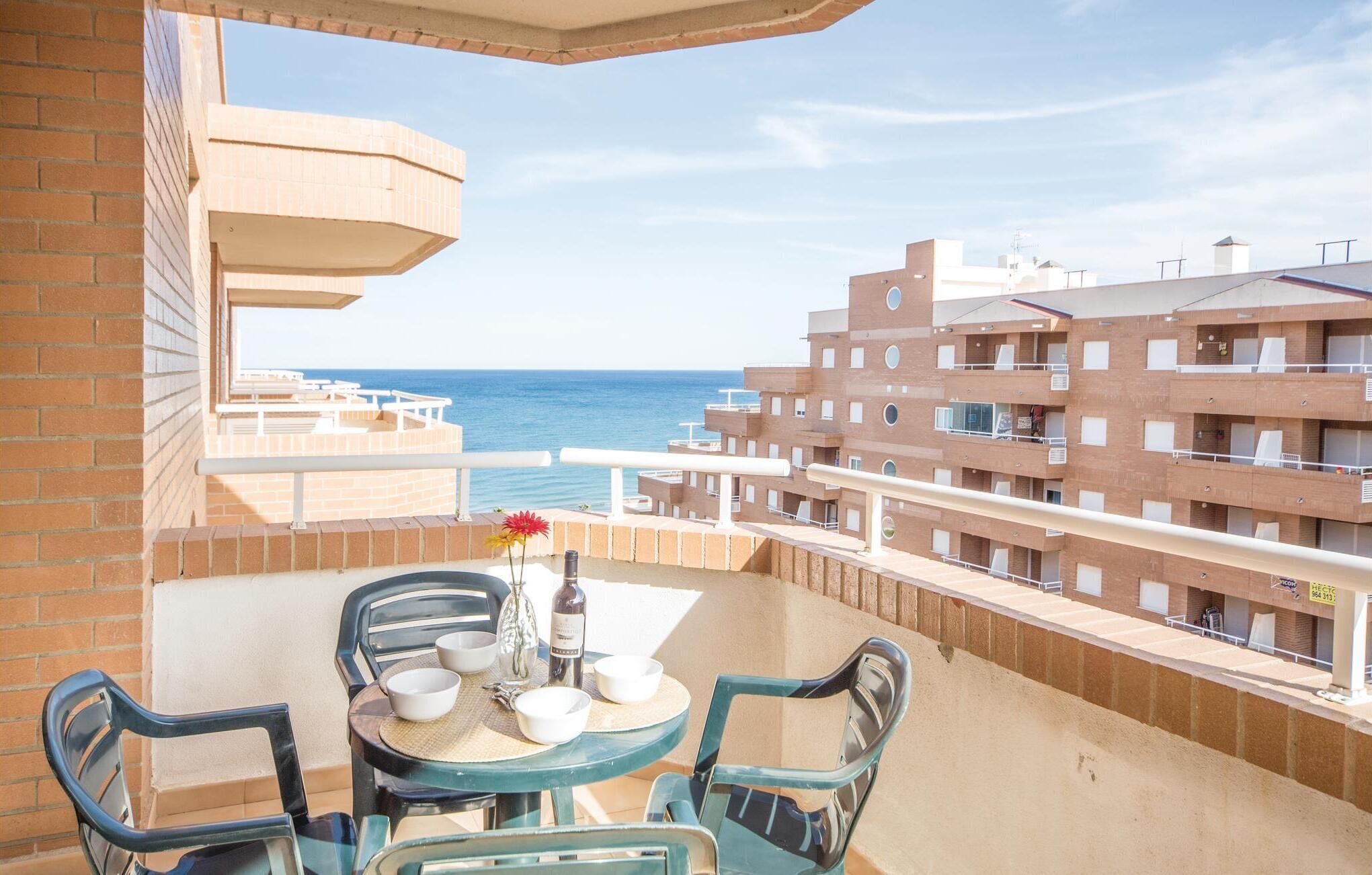 Ein Balkon mit Tisch und Stühlen mit Blick auf einen Strand und ein mehrstöckiges Gebäude.